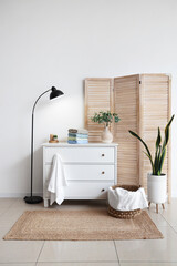 Stack of clean soft towels and vase with green branches on white chest of drawers near white wall