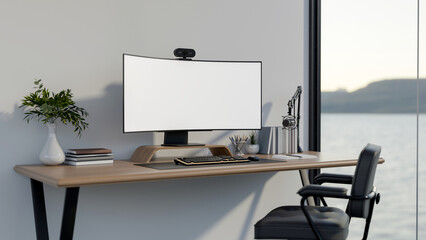 White curved screen computer with webcam and mic on wooden table and armchair in a room or office.