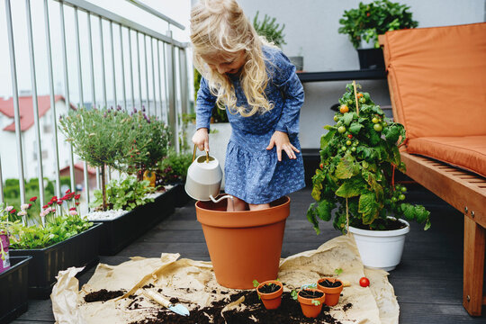 Girl standing and watering in pot at balcony