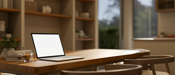 Blank screen laptop and coffee cup aside book on wooden table in a cosy style bedroom or living room.