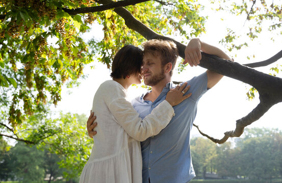 Woman embracing man with arm around branch of tree at park