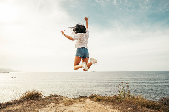 Rear view of yung woman jumping on viewpoint, Getxo, Spain