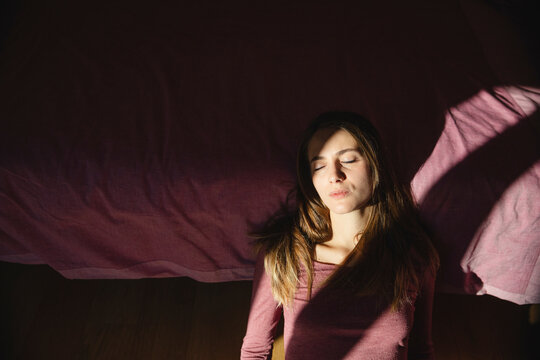 Young depressed woman with eyes closed leaning on bed at home