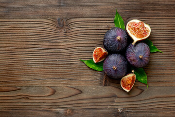 Purple ripe figs fruit and slices with green leaves top view on a wooden background