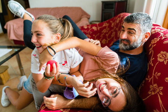 Father with two playful daughters on couch at home