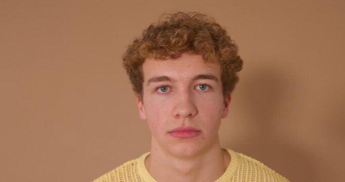  Video clip of a young adult male posing in the studio, looking at the camera and resting one hand on his face as he smiles. He has curly hair and is wearing casual clothing.
