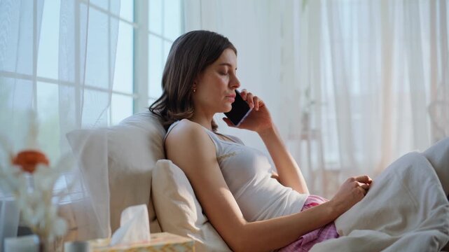 Unhealthy girl calling doctor lying in comfortable apartment bedroom. Sad woman