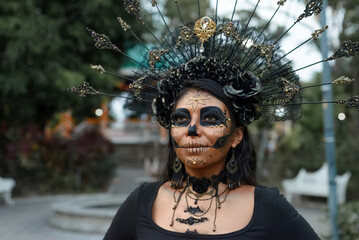 A woman adorned in elaborate Day of the Dead makeup and a stunning black and gold headdress.