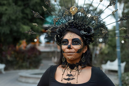 A woman adorned in elaborate Day of the Dead makeup and a stunning black and gold headdress.