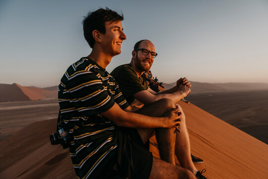 Namibia, Namib desert, Namib-Naukluft National Park, Sossusvlei, two smiling men sitting on Dune 45 at sunrise