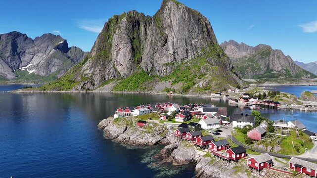 Drone flying over the car bridge and small fishing village Hamn&oslash;y in Norway towards iconic mountains above the sea with wooden drying racks for torrfisk