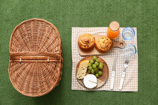 Wicker picnic basket with tasty food, glasses and bottle juice on green grass background