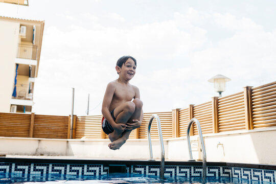 Excited boy jumping in pool against sky during summer