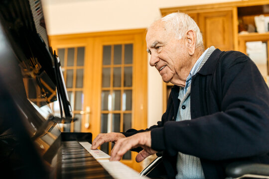Smiling senior man sitting in wheelchair playing piano at home