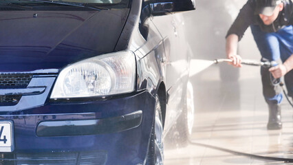 Car wash worker cleaning vehicle with high pressure water jet