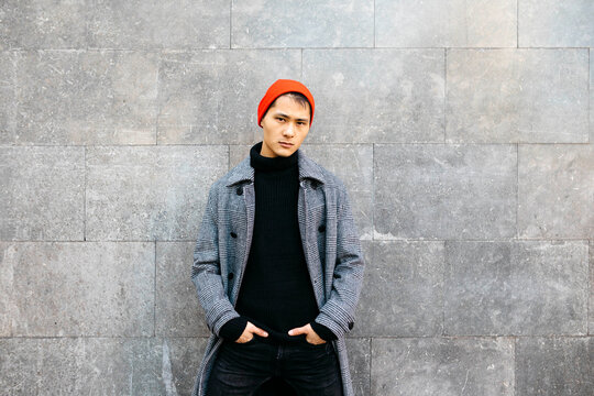 Portrait of stylish young man wearing cap, black turtleneck pullover and grey coat