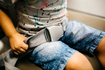 Little boy adjusting seat belt in aeroplane, partial view
