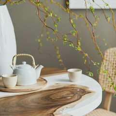 Interior design of stylish dining room interior with family wooden and epoxy table, rattan chairs, flowers in vase and teapot with cups.  Details. Template.