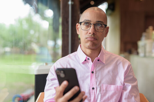 Bored businessman using phone in coffee shop rolling eyes