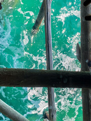 Sunlight filtering wooden pier beams, revealing turquoise waters and white seafoam along coastal Rocca San Giovanni, Abruzzo, Italy