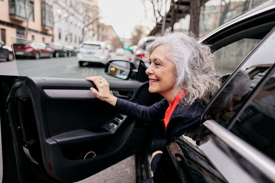 Happy mature businesswoman disembarking from car