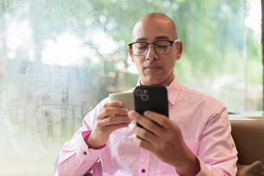 Bald Hispanic man holding coffee cup and using mobile phone in cafe