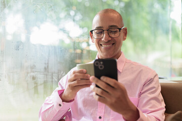 Bald Hispanic man holding coffee cup and using mobile phone in cafe