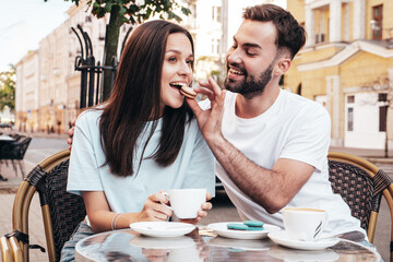 Smiling beautiful woman and her handsome boyfriend. Happy cheerful family. Couple drinking coffee in restaurant. They drinking tea at cafe in the street. Holding cup. Feeding his girlfriend