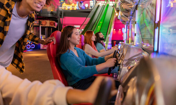 Multiracial friends playing and having fun with driving simulator in amusement arcade