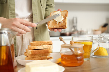 Woman spreading butter onto toasted bread in kitchen