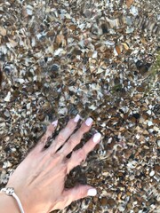 Female Hand with Manicure Touching Clear Water over Pebbles