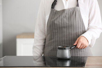 Woman putting cezve with coffee on stove in kitchen