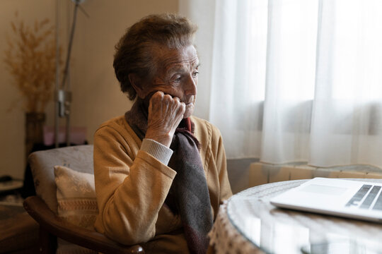 Thoughtful senior woman sitting in front of laptop at home