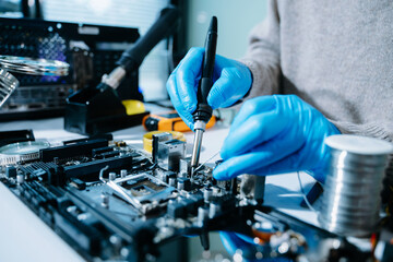 Closeup of technician soldering a computer motherboard with precision tools, showcasing electronics repair, hardware maintenance, and modern technology