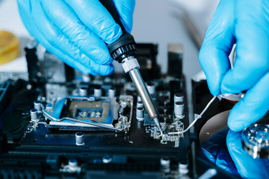 Closeup of technician soldering a computer motherboard with precision tools, showcasing electronics repair, hardware maintenance, and modern technology