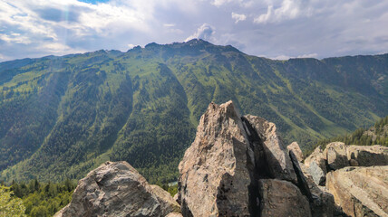 Scenic mountain scenery with green forests, gray rocks, distant snowy mountain, and cloudy sky. Nature's beauty captured in one picturesque image.