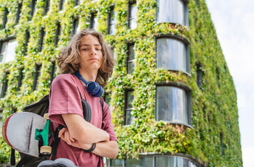 Teenager with skateboard in front of eco friendly urban green building