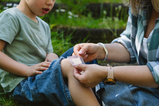 Mother applying bandage on son's knee in garden
