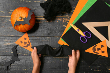 Child with supplies making Halloween decorations and origami bat on black wooden background