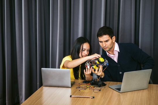 Mentor and student collaborate in workshop, assembling a robotics prototype between laptops. STEM project blends technology, innovation, engineering, teamwork, and guided collaboration.
