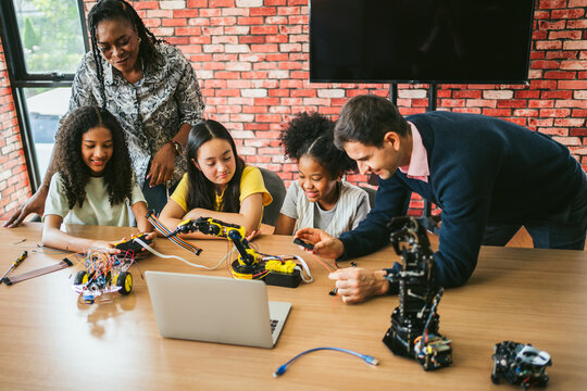 Students and mentors collaborate on robotics projects in classroom, assembling kits and coding at a table. Hands-on education blends engineering, technology, innovation, teamwork, and programming.