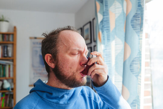 Man with eyes closed using asthma inhaler at home