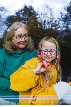 Smiling grandmother standing by granddaughter drawing heart shape on window