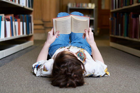 Female student reading book in a public library, lying on the ground