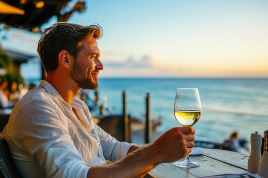 Relaxed man enjoying white wine by the ocean during sunset