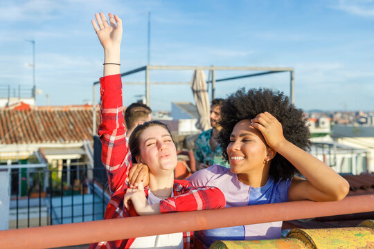 Cheerful young female friends standing by railing on rooftop