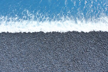 Dark gray pebbles meet a bright blue ocean