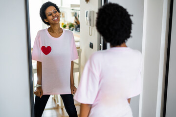Happy young woman wearing t-shirt with heart shape looking in mirror