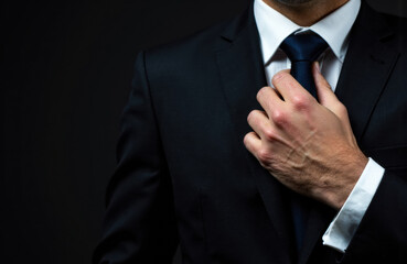 Businessman adjusting his tie in formal suit and shirt on dark background