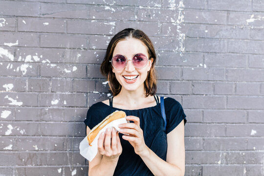 Portrait of smiling woman with Hot Dog in front of wall
